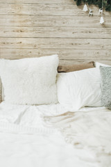 Bed with white pillows and bedcovers at wooden wall. Modern bedroom interior design.
