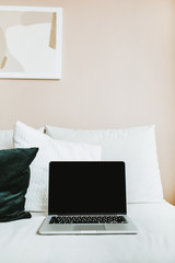 Minimal home office workspace. Laptop with mock up screen on bed with pillows. Blogger / freelancer business concept.