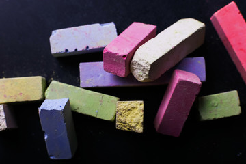 Multicolored crayons lie on a black chalkboard, copy space, macro. The concept of school, education and childhood.