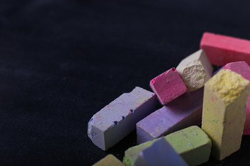 Multicolored crayons lie on a black chalkboard, copy space, macro. The concept of school, education and childhood.