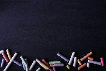 Multicolored crayons lie on a black chalkboard, copy space. The concept of school, education and childhood.