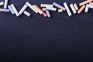 Multicolored crayons lie on a black chalkboard, copy space. The concept of school, education and childhood.