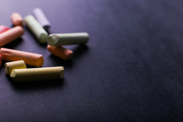 Multicolored crayons lie on a black chalkboard, copy space, macro. The concept of school, education and childhood.
