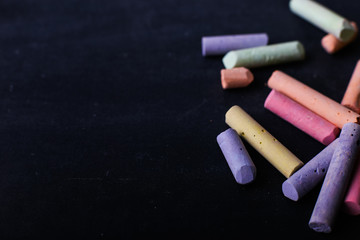Multicolored crayons lie on a black chalkboard, copy space, macro. The concept of school, education and childhood.