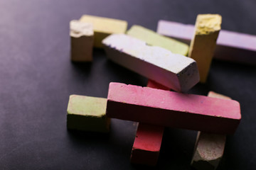 Multicolored crayons lie on a black chalkboard, copy space, macro. The concept of school, education and childhood.