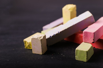 Multicolored crayons lie on a black chalkboard, copy space, macro. The concept of school, education and childhood.