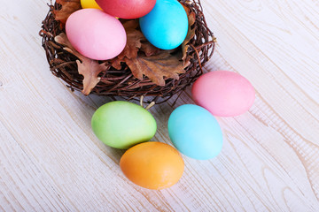 Colored Easter eggs in a nest, on a white wooden table.