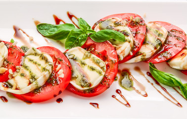 Caprese salad with mozzarella, tomato, basil and balsamic vinegar arranged on white plate