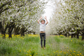 cute happy boy of 6-7 years old in a white stylish shirt, and a hat on nature in the blooming cherry apple garden of early spring