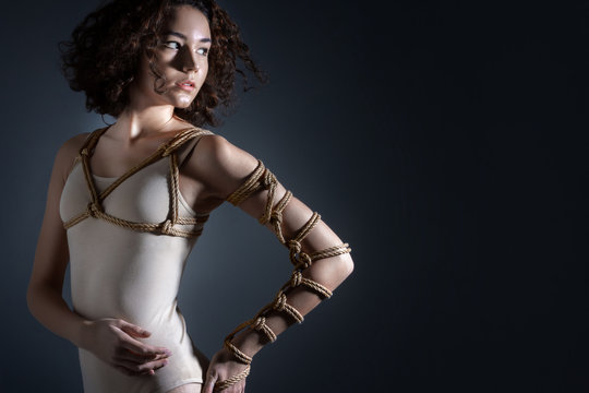 Beautiful fashion brunette woman with tied chest and hand with decorative knots of natural jute ropes. Ancient Japanese art of aesthetic bandage and tying shibari kinbaku. Sexual underwear concept.