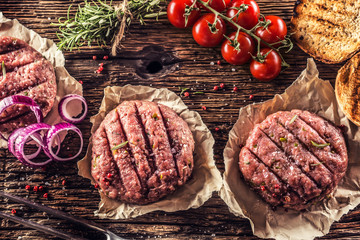 Raw burgers on wooden table with onion tomatoes herbs and spices - obrazy, fototapety, plakaty