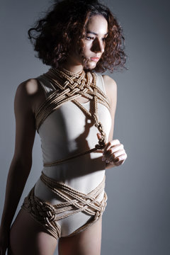 Young cute sexy sensual brunette woman female adult in beige bodysuit desires sexual tying shibari rope kinbaku japanese bondage over body. Sexual sensitive bdsm art erotic sadism dominance concept.