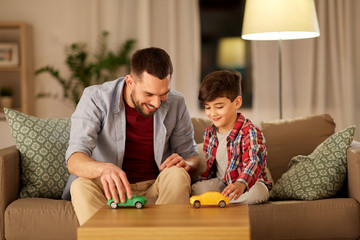 family, fatherhood and people concept - happy father and son playing with toy cars at home in...