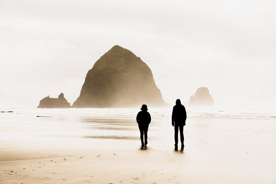 Couple walking on the beach and Haystack Rock in the background, Cannon Beach, Oregon
