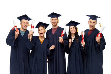 education, graduation and people concept - group of happy graduate students in mortar boards and bachelor gowns with diplomas over white background