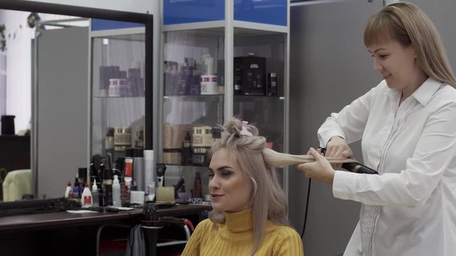 Positive Female Hairdresser Doing Hairstyle To Blonde Girl