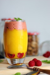 Glass of sweet delicious homemade layered smoothie dessert made from fruits and berries. Mango and orange smoothie with raspberries ice cream. Close up. Healthy breakfast.