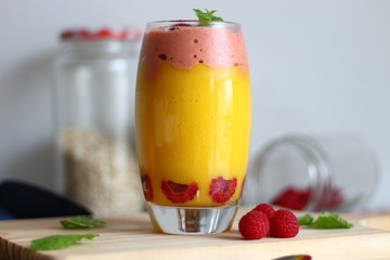 Glass with tasty mango smoothie and raspberry ice cream on wooden table.