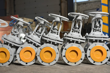 Several new gray valves, for water or gas, lie on the floor at the factory. The valves are gray for...