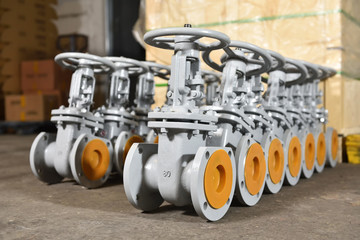 Several new gray valves, for water or gas, lie on the floor at the factory. The valves are gray for...