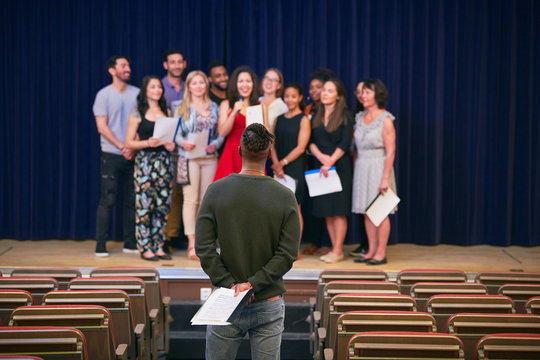 Male conductor listening to choir in auditorium