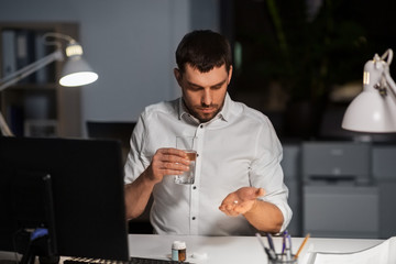 business, overwork and deadline concept - businessman taking medicine pills at night office