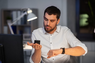 business, technology and internet of things concept - businessman using smart speaker and watch at night office