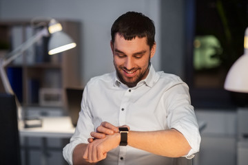 business, technology and time management concept - happy smiling businessman with smart watch at nigh office