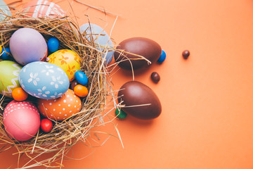 Colorful easter eggs with chocolate and candies in a nest on a orange background