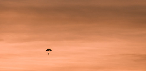 Silhouette of parachutist flying slowly on parachute in the beautiful sky at sunset.