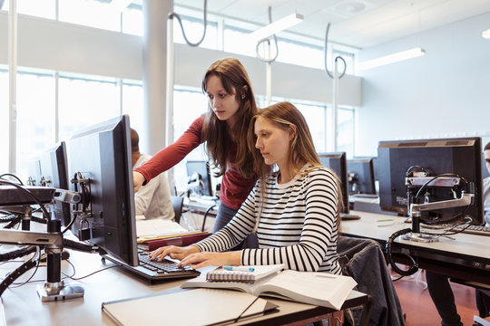 Woman assisting friend while using desktop computer in library
