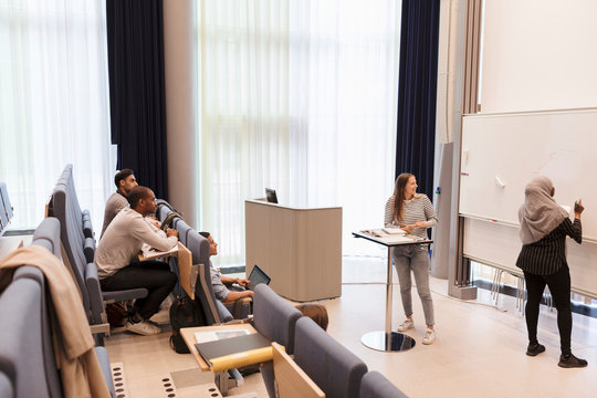 Students looking at friend writing on whiteboard during rehearsal in lecture hall