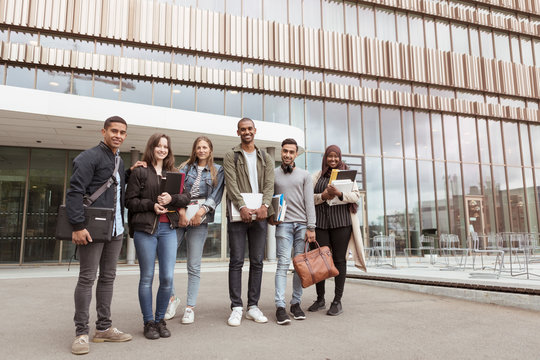 Full length portrait of smiling multi-ethnic students standing against building in campus at university