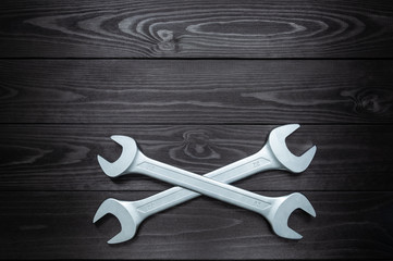 Crosshair of two chrome wrenches on dark wooden workbench.