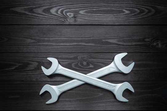 Crosshair of two chrome wrenches on dark wooden workbench.