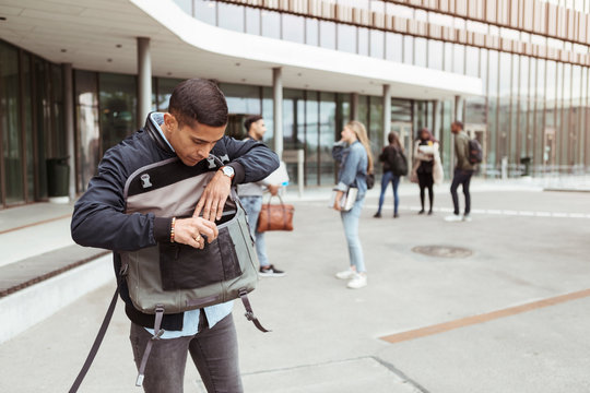 Young student searching in bag while friends standing in background at university
