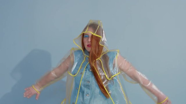 ginger hair woman in transparent raincoat with pop art bright makeup dancing with strange movements.
