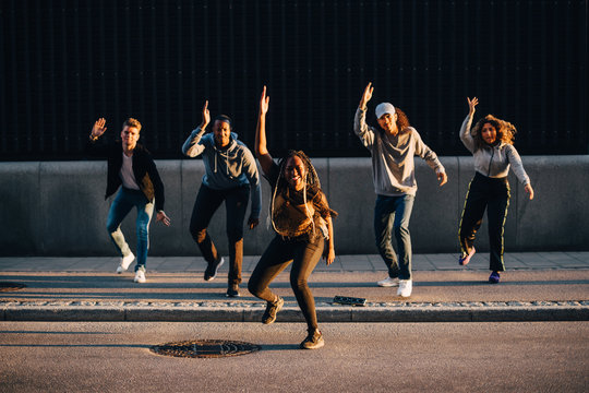 Full length of multi-ethnic friends dancing on sidewalk in city