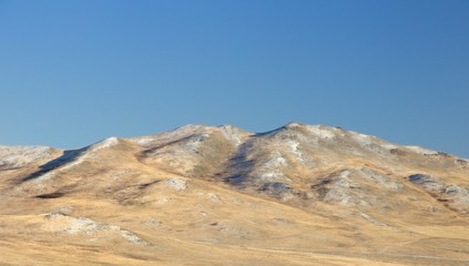 Winter landscape with a smooth hills covered with a yellow dry grass and first snow under dark blue sky in Khakassia, Russia