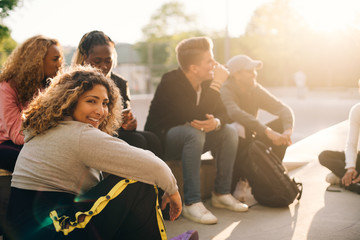 Portrait of smiling young woman sitting with friends at skateboard park