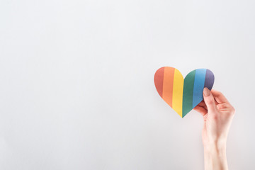 cropped view of female hand with rainbow colored paper heart on grey background, lgbt concept