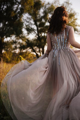 Fototapeta premium Wedding near the river in field at sunset with brown horse. Bride in light airy dress in color of dusty rose. Beige dress with sparkles. Light suit with bow tie. bride and groom embrace and kiss.
