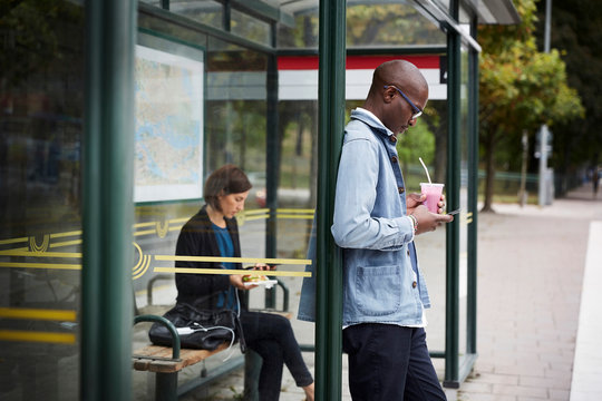 Side view of man using smartphone at bus stop