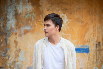 Naklejka na ściany i meble Asian man in casual clothes standing on old wall background.