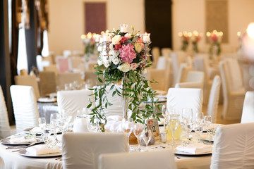 Beautiful white round table at the restaurant. Wedding reception day. Champagne and floral composition