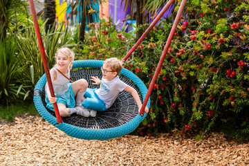 Two children boy and girl playing in the park with swing