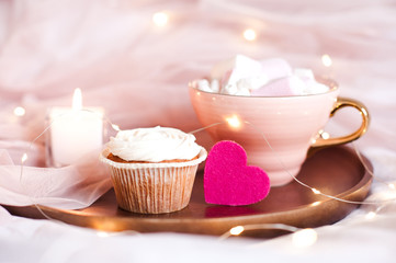 Creamy muffin with pink heart and cup of coffee over lights at background. Good morning.