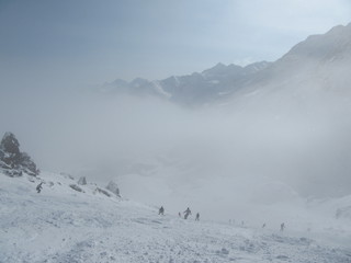 Skiers and snowboarders down the ski slope in a heavy fog, which is very dangerous.