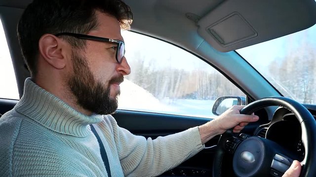 A man drives a car in winter on the highway between cities. Close up profile shot