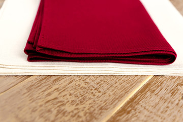 close up of cloth napkins of beige, and burgundy colors on rustic brown wooden table. Shallow depth of field.